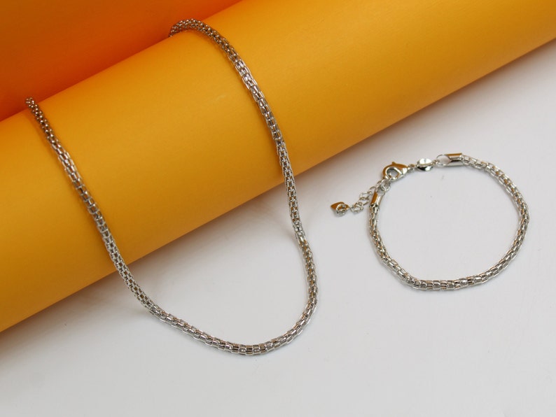 A matching silver mesh chain necklace and bracelet rest on a dual-toned orange and white surface.