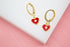 A pair of gold huggie hoop earrings features hanging red enamel heart charms with central crystal stones.