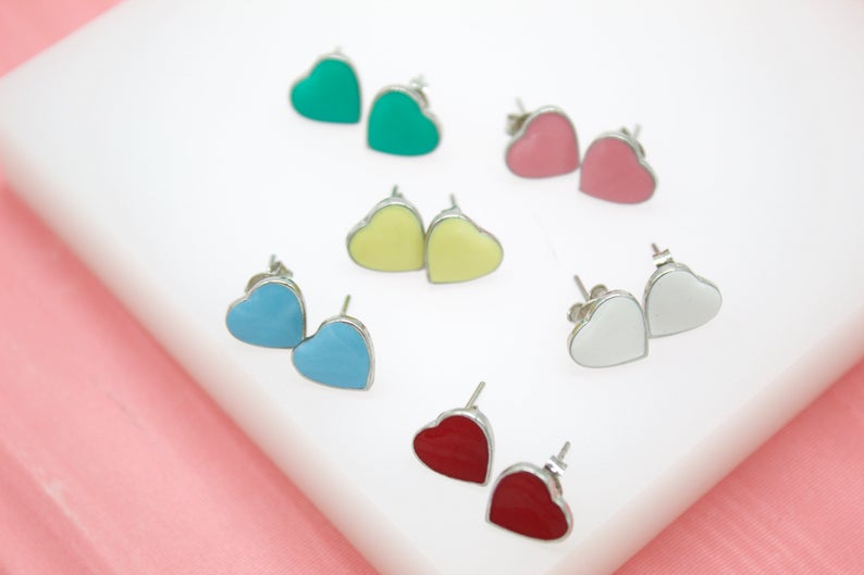 Several pairs of colorful heart-shaped stud earrings in turquoise, pink, yellow, blue, white, and red are arranged on a white display block.