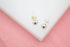A pair of polished silver ball stud earrings rests on a white display surface against a pink background.
