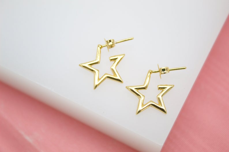 A pair of shiny gold star-shaped stud earrings rests neatly on a white and pink display surface.