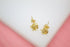 Two intricate gold knot stud earrings rest against a clean white and pink background.