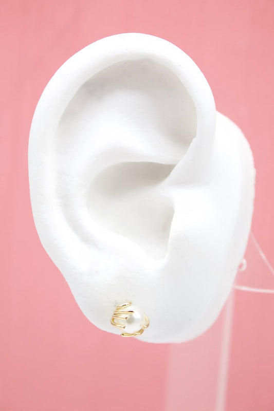 A white ear mannequin displays a gold wire-wrapped pearl stud earring against a pink background.
